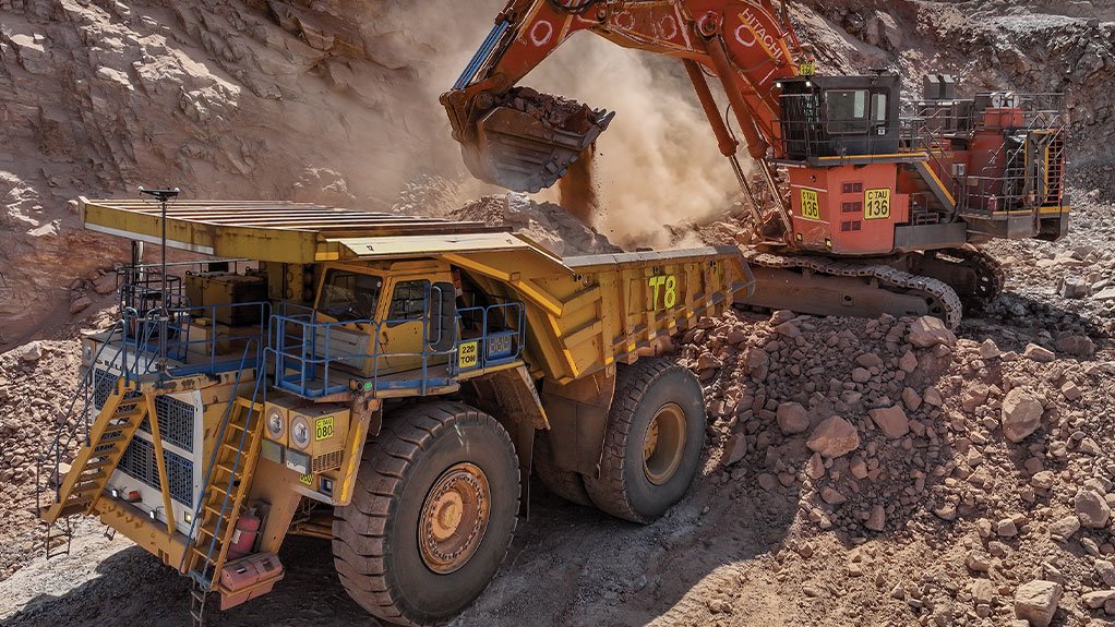 Excavator loading a haul truck with ore at an open cast pit, dust rising