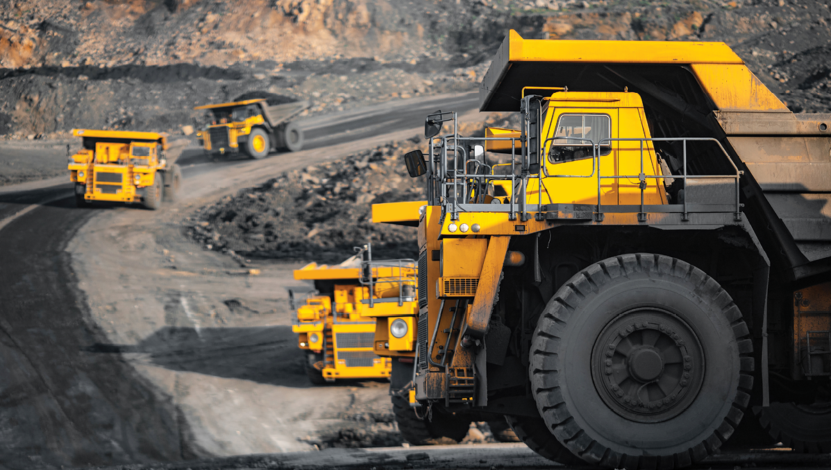 A line of yellow haul trucks moving along a maintained haul road