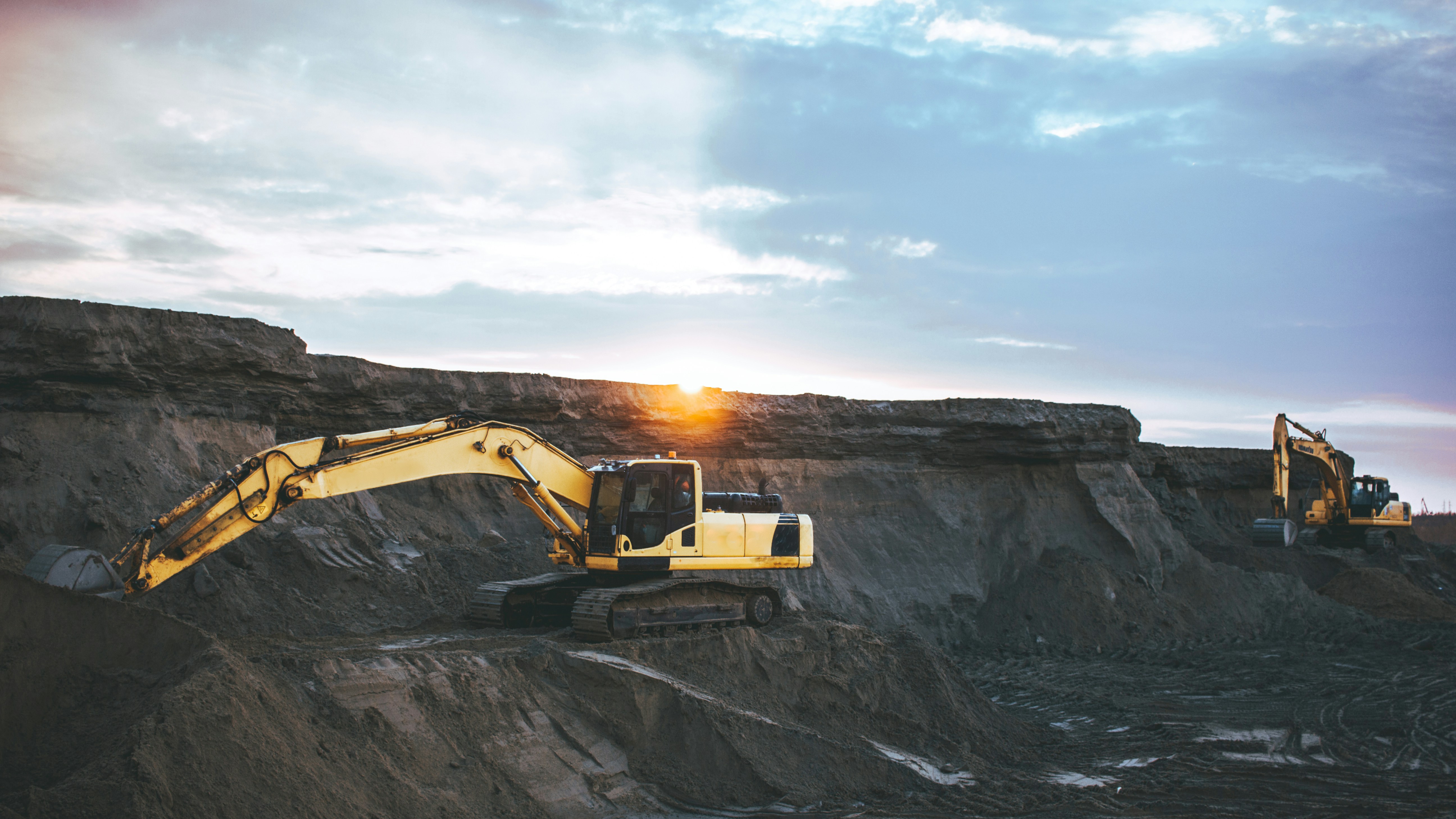 Two excavators working a sunset earthworks site with terraced ground